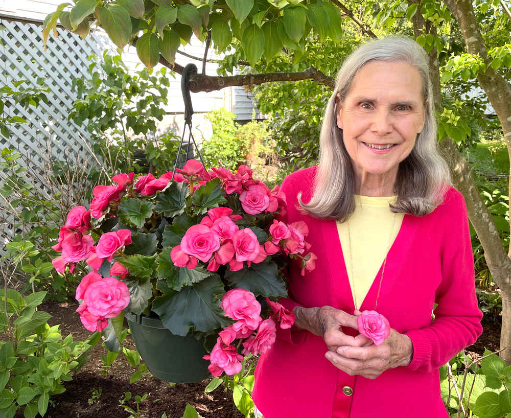 Alexandra in a bright pink sweater next to a large hanging basket full of pink begonias