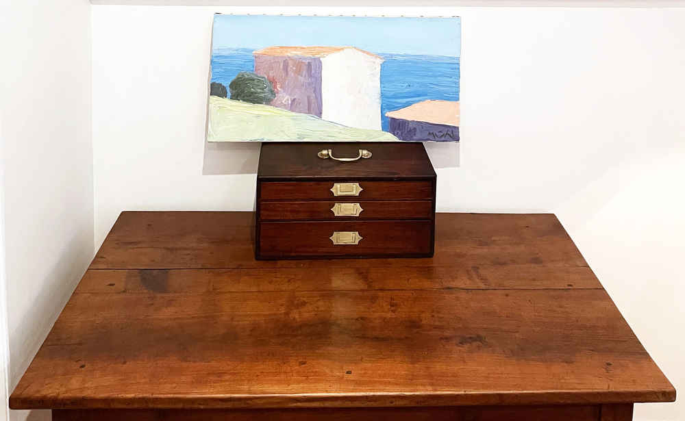 A wooden box and painting sit atop an otherwise empty table.