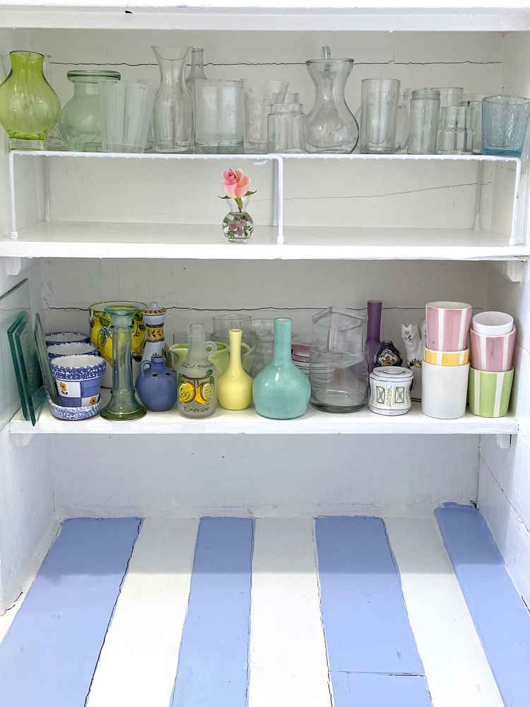 A photo of Alexandra's pantry, where one shelf is empty except for a vase with a pink rose.