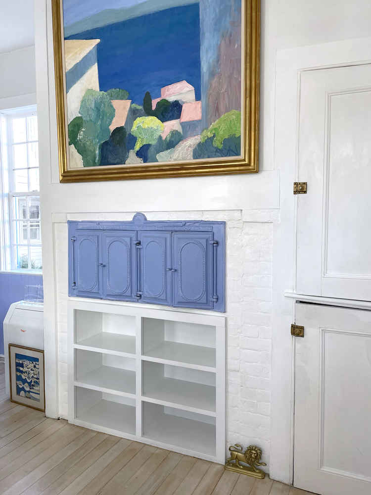 Empty shelves in Alexandra's white kitchen, with a painting above them.