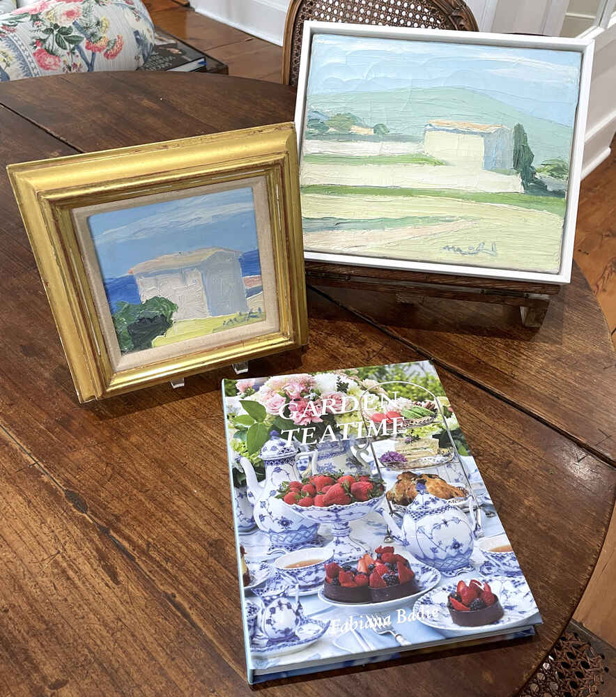 Two Muhl paintings next to a book on a wooden table