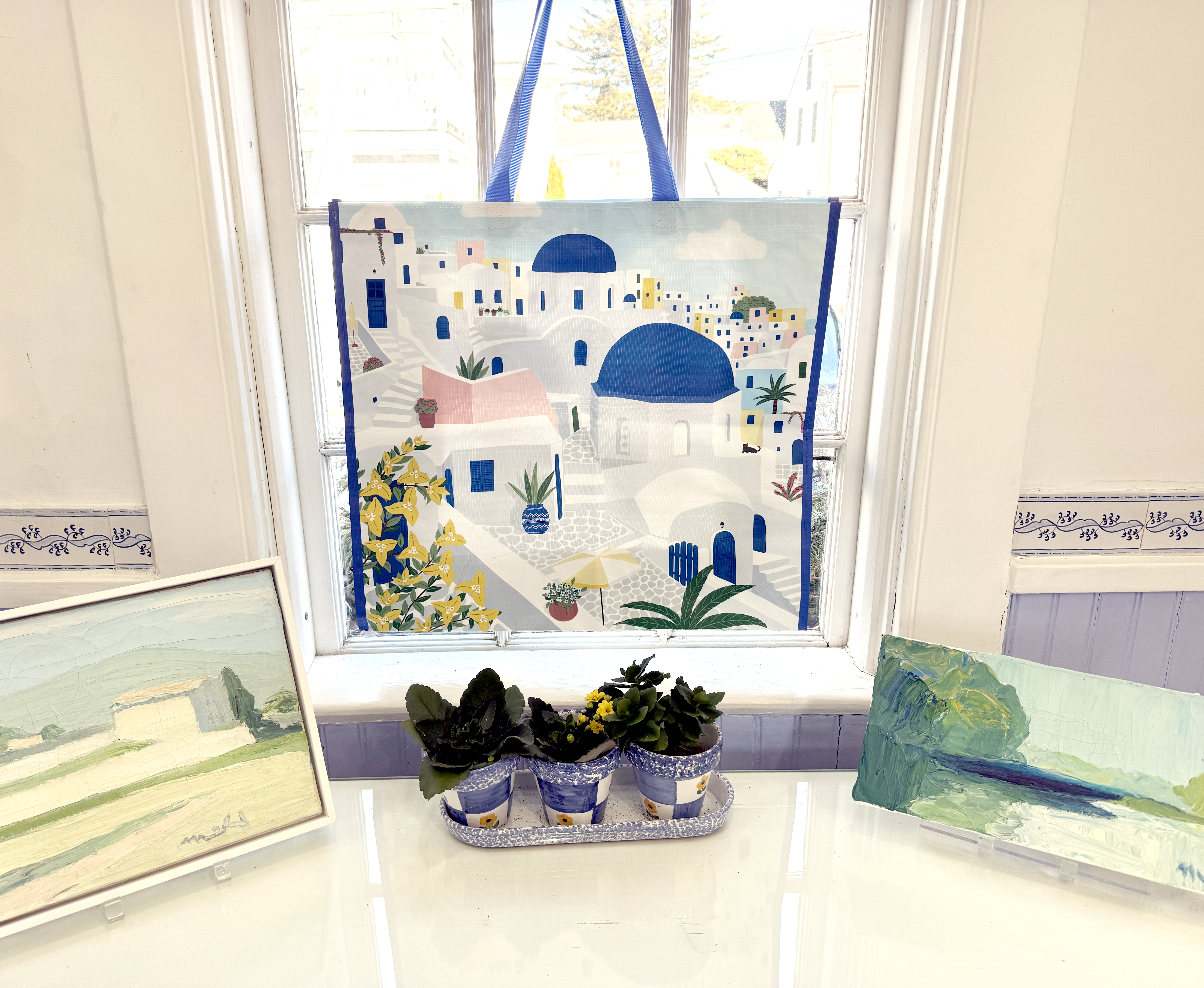 A shopping bag with a Greek scene on it hanging from the window