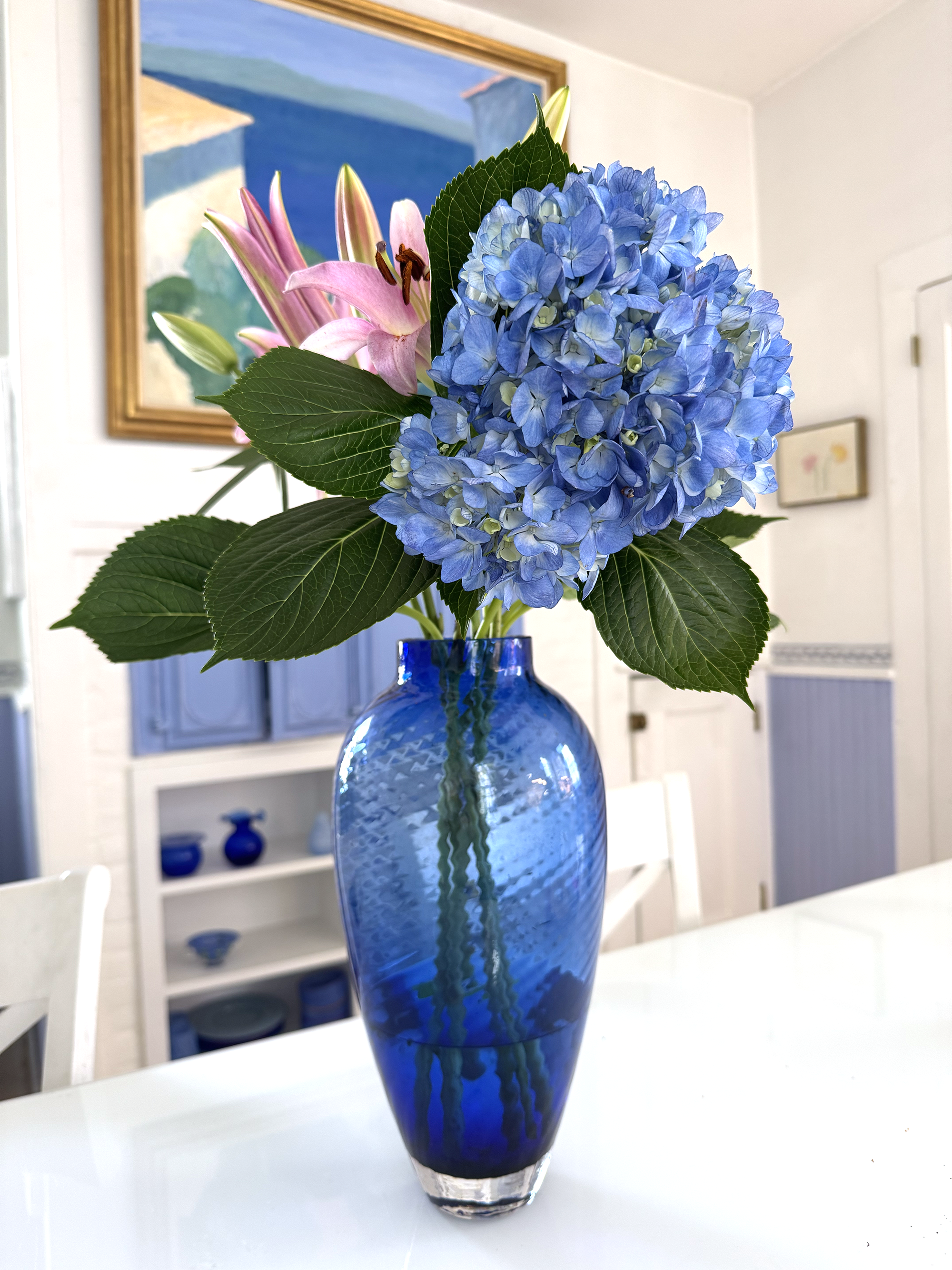 A blue vase with blue hydrangea and pink lilies on the kitchen table.