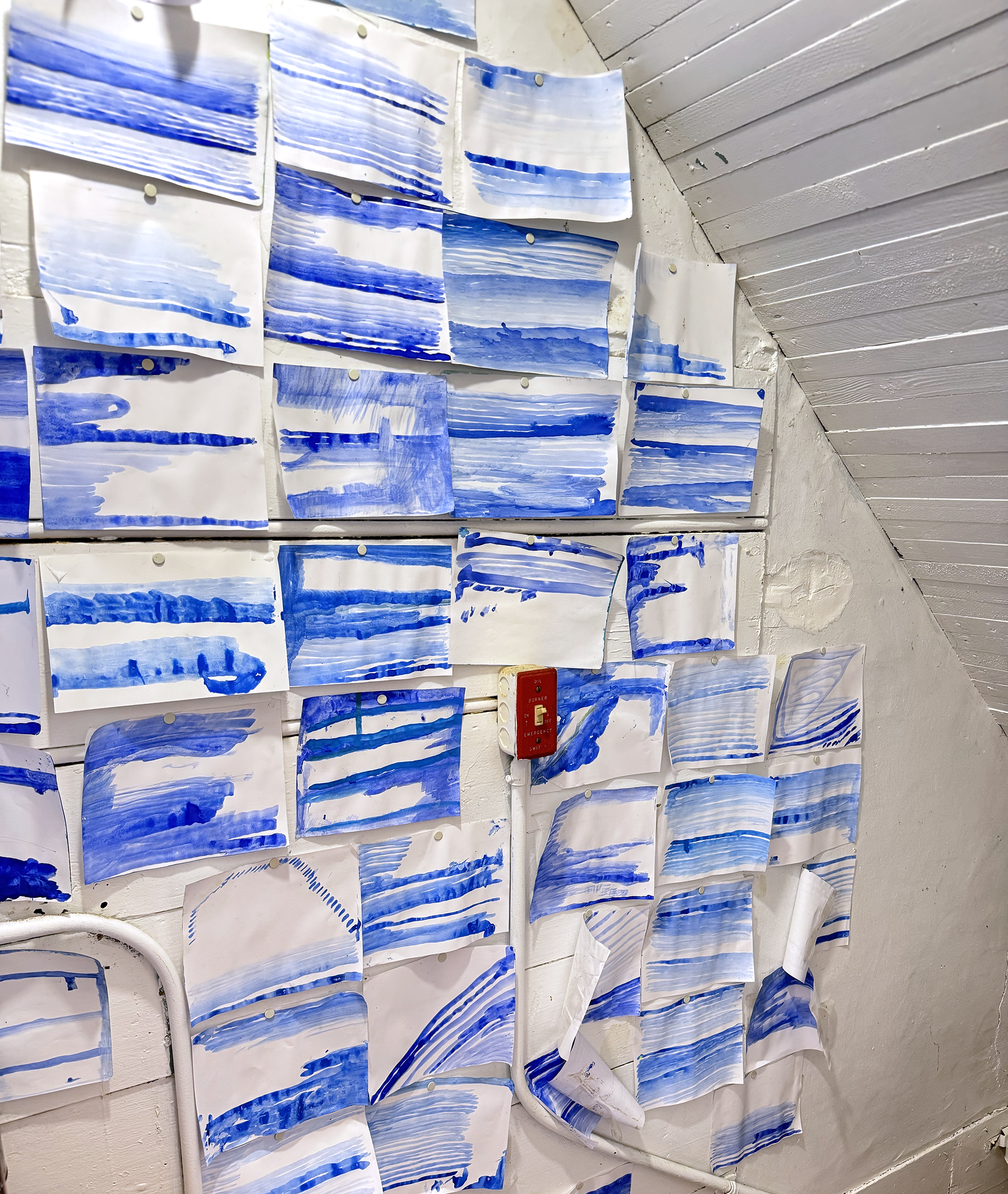 Dozens of blue and white watercolor seascapes tacked to a stairway wall.