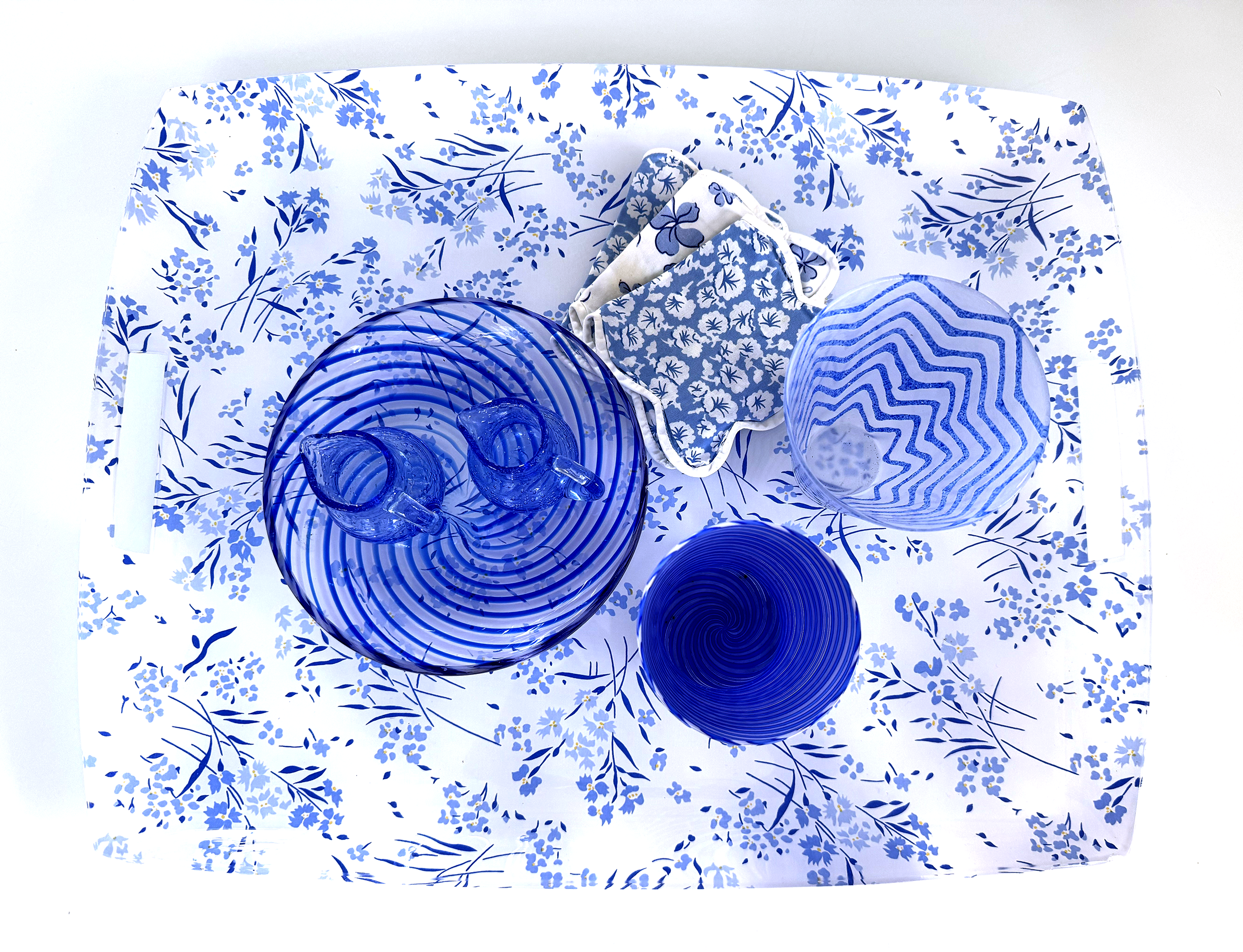 A blue and white flower print tray with an assortment of blue glassware on top.