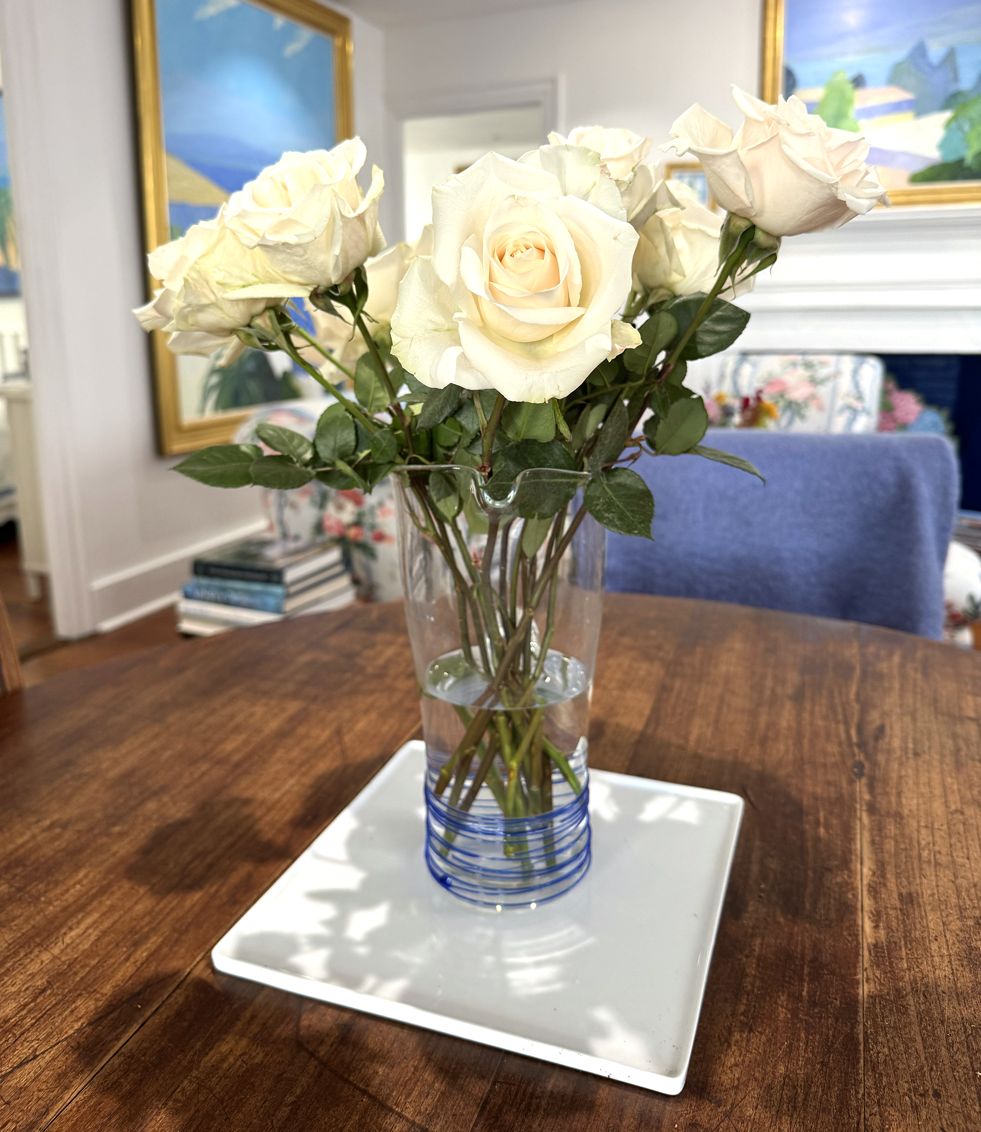 White roses in a clear vase on a wooden table.